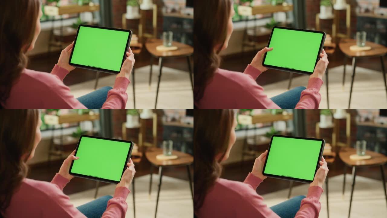 带有绿屏模拟显示的平板电脑上的女性滚动内容。女人在家放松，在移动设备上阅读社交媒体帖子。特写镜头。