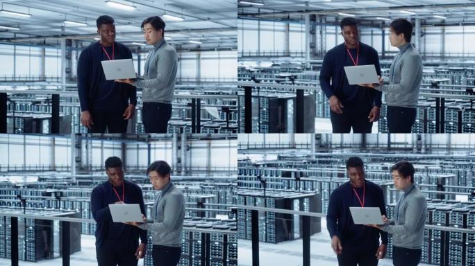 两名多种族男性数据中心系统管理员和IT专家交谈，使用笔记本电脑。信息技术工程师在云计算服务器场中从事