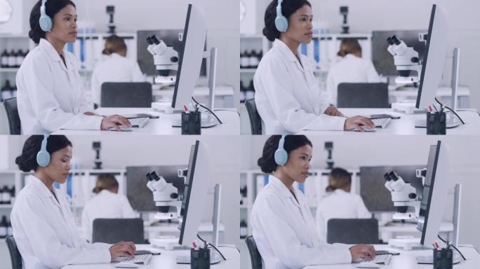 科学家在实验室工作时使用计算机并在无线耳机上听音乐。在医学研究设施中使用技术的重点病理学家和生化工程
