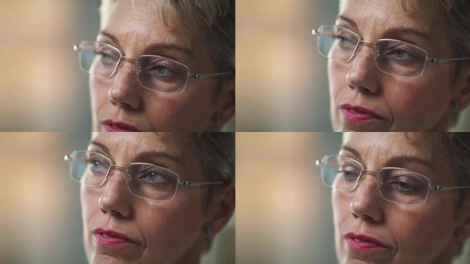 4k视频片段，一名戴着眼镜的高级妇女坐在家里时看起来很体贴