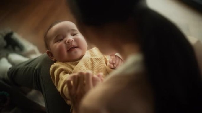 一个可爱的亚洲婴儿的肖像笑着，躺在母亲的腿上，一起享受着一段亲密的时光，带着爱看着她。顽皮的妈妈给她