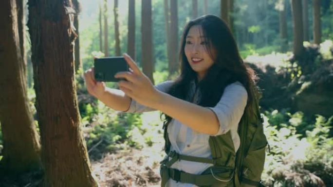 年轻女子与移动phine在森林中徒步旅行自拍照