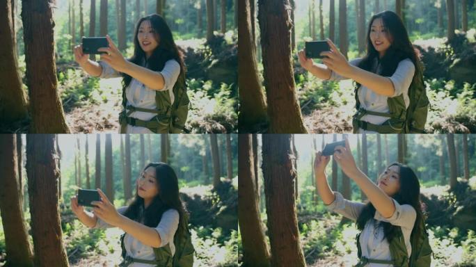 年轻女子与移动phine在森林中徒步旅行自拍照