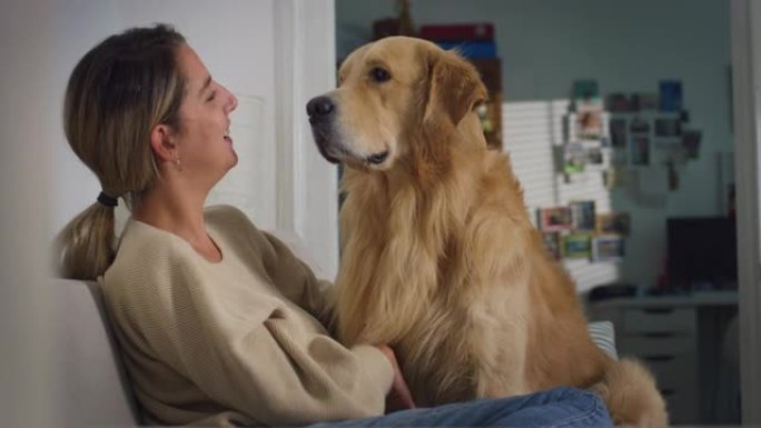 美丽年轻女子的肖像在家里拥抱她可爱的金毛猎犬。女孩和她的狗玩耍，最好的朋友。她宠物抓挠超级快乐的狗狗