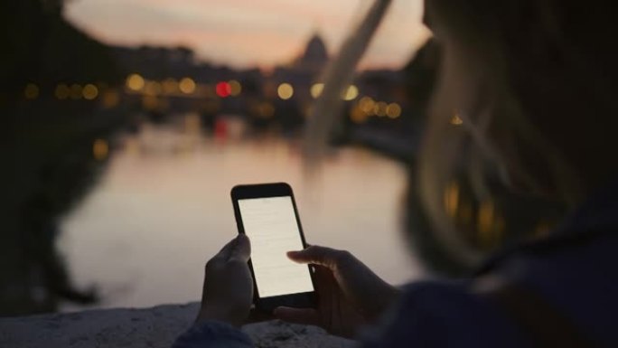 黄昏时，SLO MO女人在圣安吉洛桥对面的桥上使用智能手机