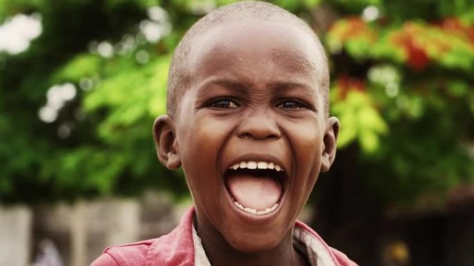 一个富有表现力的真实非洲孩子的特写肖像，笑着看着模糊的相机背景。快乐，精力充沛，充满活力的黑人男孩快