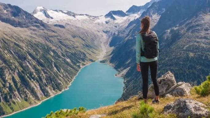 健康导向的女人站在山顶上，欣赏周围群山和绿松石湖的壮丽景色