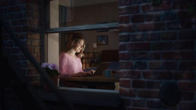 Night Dolly Shot: 年轻的女性电子商务项目经理在家中使用笔记本电脑工作，在与同事在线