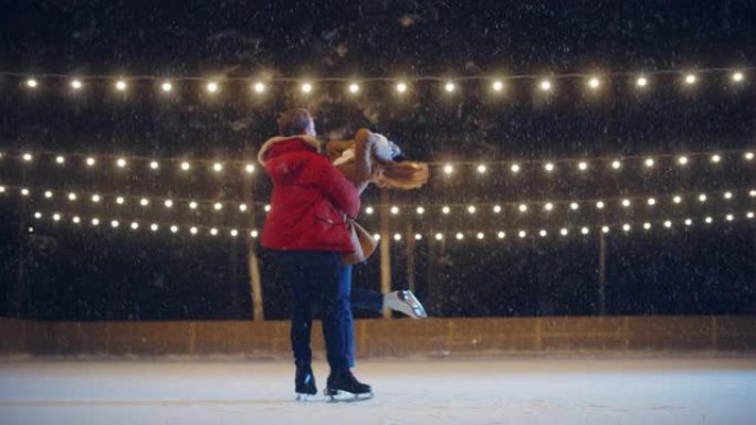 浪漫的冬夜: 滑冰夫妇在溜冰场上玩得开心。美丽的雪落在双人滑冰男孩和恋爱中的女友上，跳舞，牵手，拥抱