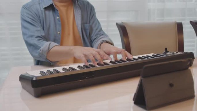 特写年轻的亚洲男性通过互联网上的视频通话与他的朋友在数字平板电脑上玩电子钢琴或键盘电话会议。玩音乐的