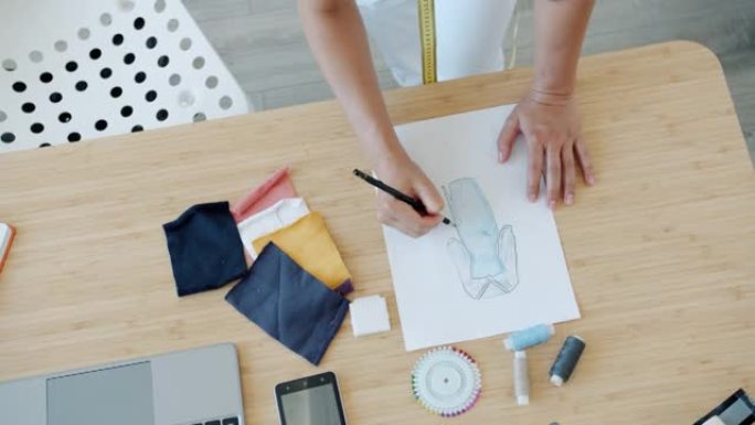 女设计师的手的特写在桌子上的纸上绘制新潮衣服的草图