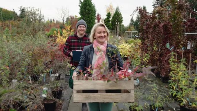 高级妇女在其花园中心的推销员协助下购买植物