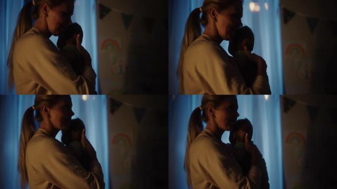 快乐的母亲晚上在舒适的黑暗儿童卧室里抱着可爱的新生婴儿。有爱心的妈妈拥抱着新生的小孩，他们在睡觉前就