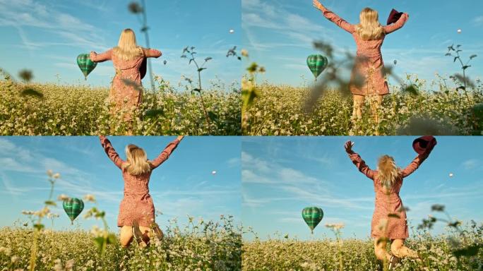 超级慢动作女人在飞着的热气球前的花田里跳
