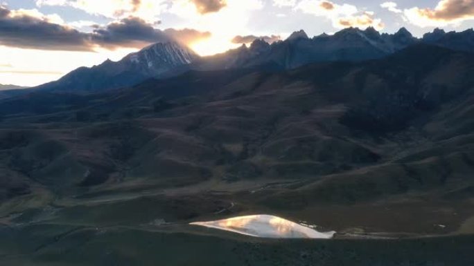 夕阳从雪山后落下，映照着草原上小湖的金黄色