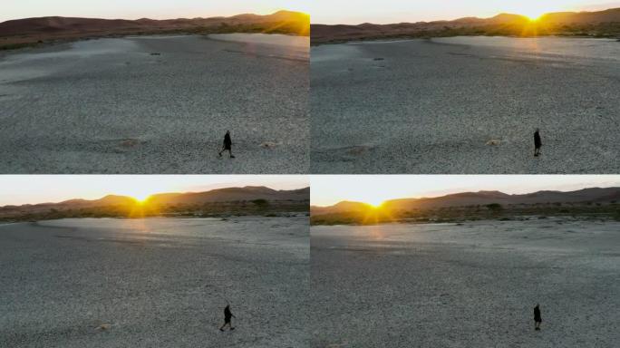 气候变化。由于气候变化和全球变暖造成的干旱，一名饱受摧残的农民在日落时走过干燥大坝的图案破裂的泥面的