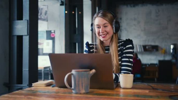 团结和隔离。美丽快乐的年轻金发30多岁的女人在阁楼咖啡馆用笔记本电脑网络摄像头和朋友交谈。
