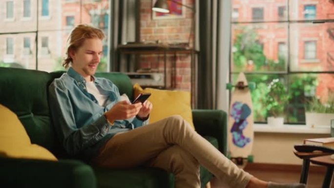 年轻英俊的成年男子坐在客厅的沙发上，放松并使用智能手机。有创意的男性检查社交媒体，与朋友聊天，浏览互