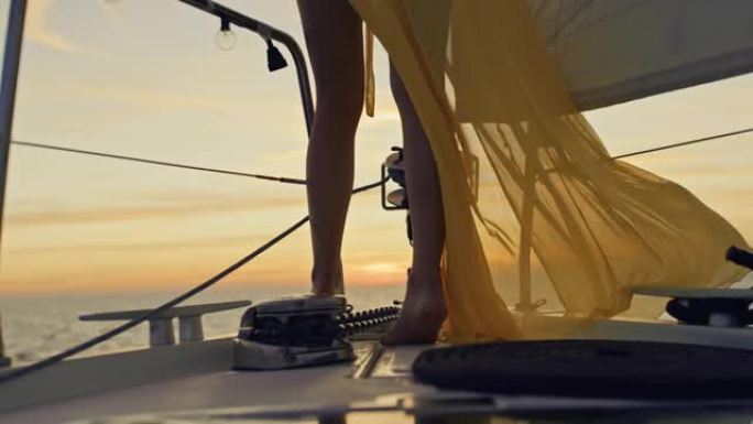 穿着黄色长裙的SLO MO无法辨认的女人在日落时享受帆
