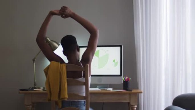 非裔美国妇女在家工作时使用计算机伸展手臂的后视图