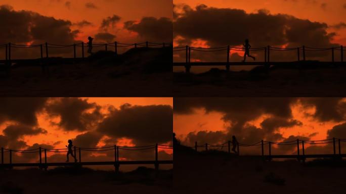 慢动作，在深橙色的日落中，无法辨认的女性在海滩上的木板路上奔跑的照片