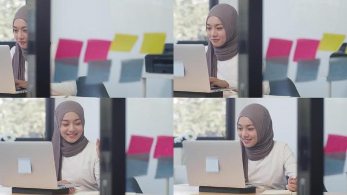 美丽的亚洲穆斯林女士休闲服在现代新的普通办公室使用笔记本电脑工作。