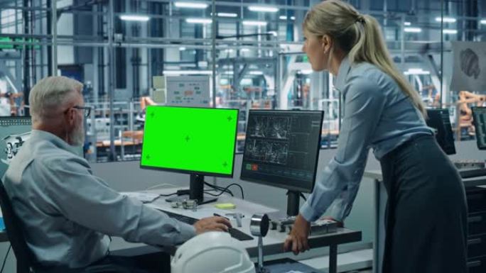 汽车工厂监控办公室: 女项目经理与在绿屏色度关键计算机上工作的男总汽车工程师交谈。自动机械臂装配线制