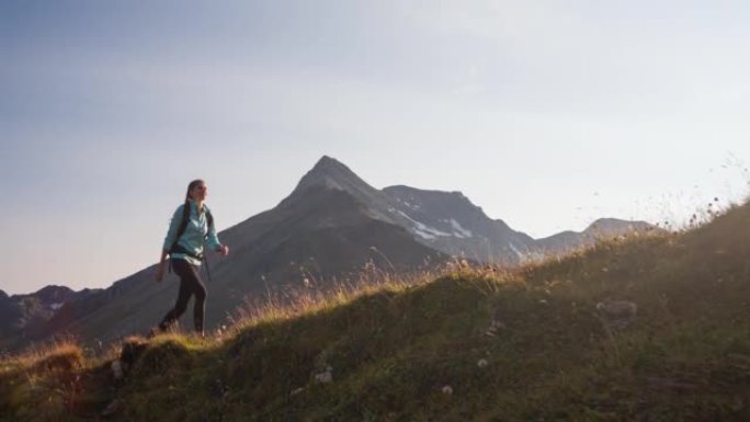 年轻的女徒步旅行者走在被山峰包围的山脊步道上