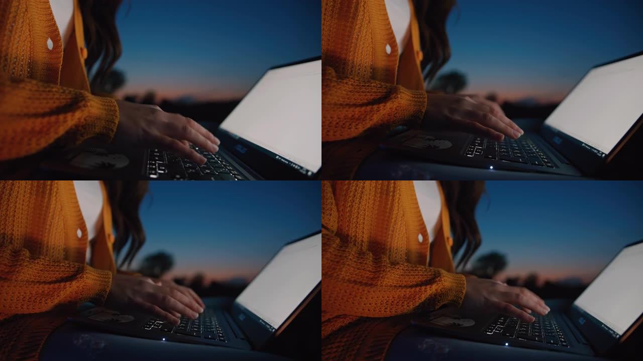 一个无法辨认的中年黑发女人坐在户外时在笔记本电脑上打字的特写慢动作，背景是黄昏的天空