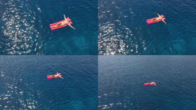 空中女子在漂浮在绿松石海上的泳池筏上放松