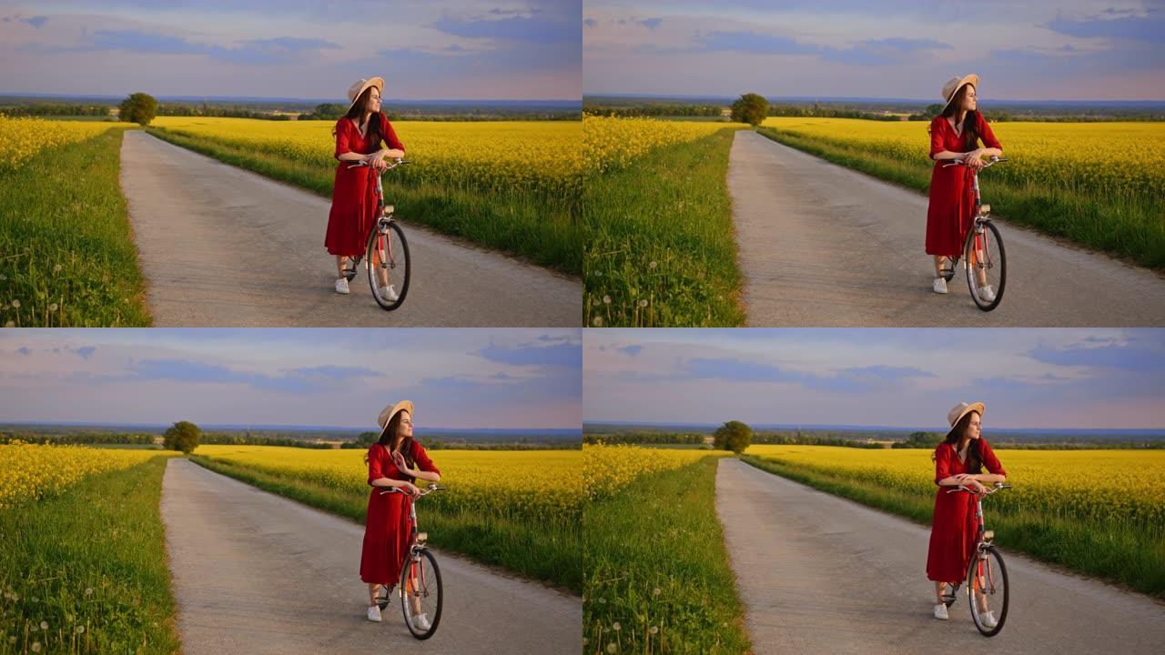 穿着红色连衣裙的美丽黑发女人，骑着自行车站在草地上，享受着金色的日落，上面种满了黄色的花朵，慢动作
