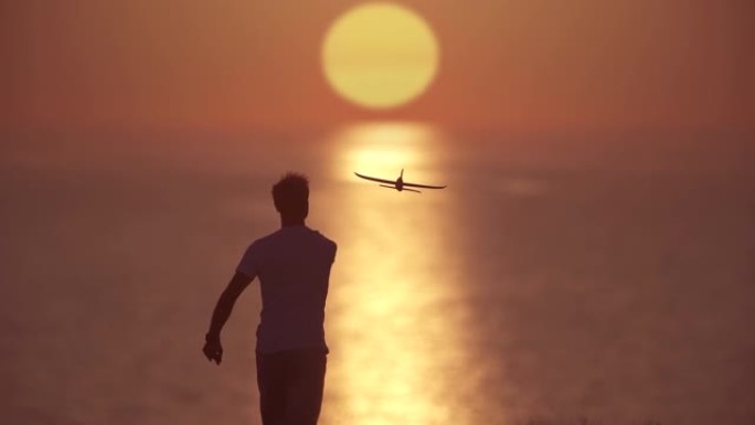 那个把玩具飞机扔在日落背景上的人。慢动作