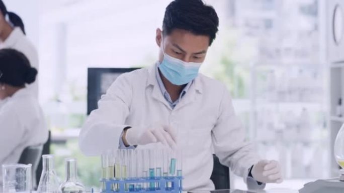 年轻的男性生物学家在COVID研究实验室将试管结果输入数字平板电脑。戴着口罩的科学家或化学专家，在临