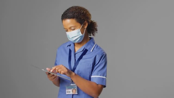女护士穿制服和戴口罩的工作室肖像，使用数码平板电脑