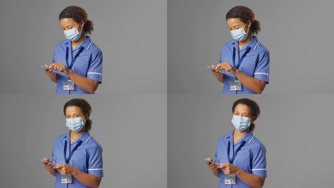 女护士穿制服和戴口罩的工作室肖像，使用数码平板电脑