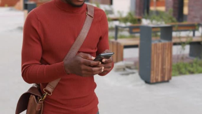 非裔美国商人在市区散步时使用智能手机