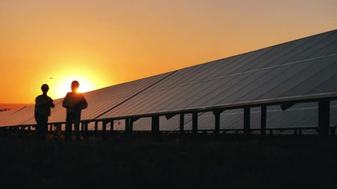 两名安全检查员在日落时分路过太阳能电池。可再生电力概念。