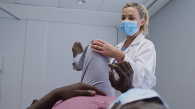 多元化的女性骨科医生在口罩上检查男性患者