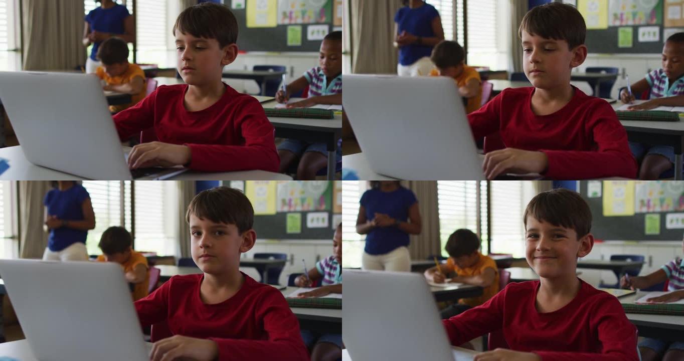 快乐的高加索男生的肖像坐在教室里，使用笔记本电脑，看着相机