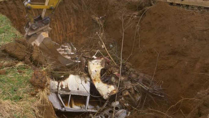 特写: 挖掘机铲斗在废料场附近的一个洞里压碎了一辆生锈的旧车。