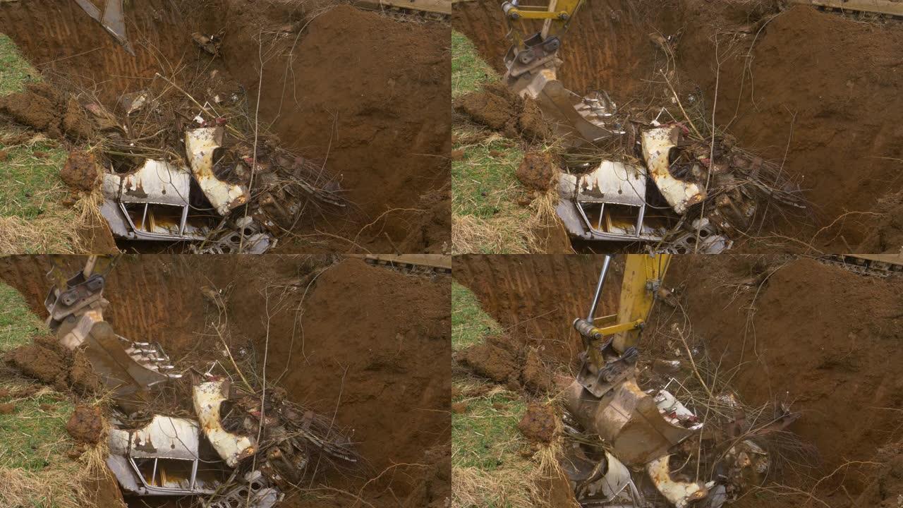 特写: 挖掘机铲斗在废料场附近的一个洞里压碎了一辆生锈的旧车。