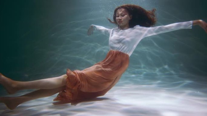 自然美概念。年轻美丽的混血女子潜水的电影肖像，在水下慢动作下摆姿势。