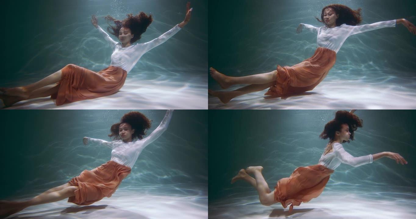 自然美概念。年轻美丽的混血女子潜水的电影肖像，在水下慢动作下摆姿势。