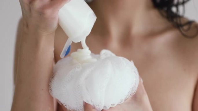 年轻裸女在粉扑上涂抹保湿沐浴露。