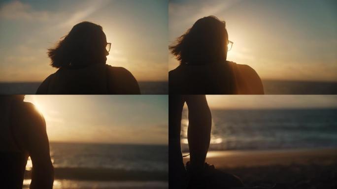 特写镜头的人坐在冲浪板旁边的海滩上，在暮色中看着大海，后视