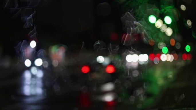夜间城市交通穿过潮湿的车窗。过往汽车的抽象波克灯。多雨的秋天天气。慢动作4K