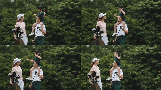 亚洲华裔年轻家庭高尔夫球手在绿色球场的结合时间，而父亲则将女儿抱在肩上