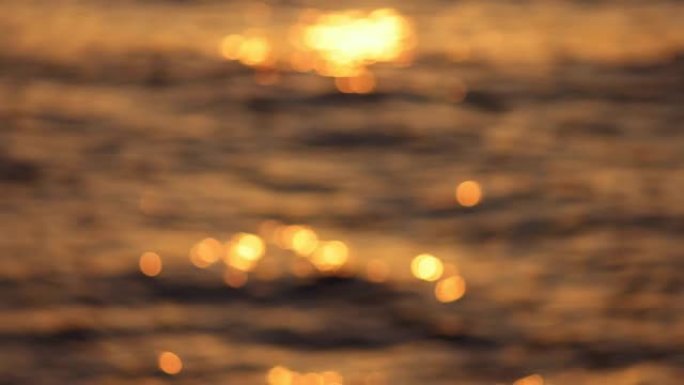 日落时海浪的模糊抽象镜头。金色的bokeh圆圈在海浪上闪闪发光。海上日落，浪漫舒适的氛围。慢动作，4