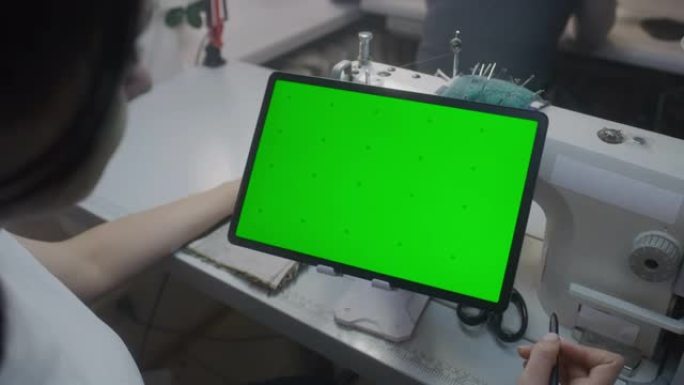 Seamstress手握手握手写笔，并在带有绿色屏幕的平板电脑上观看