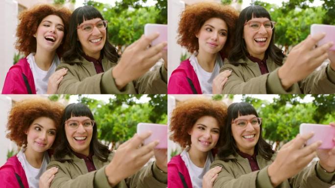 顽皮的女性朋友在城市公园外面用手机自拍。快乐的女孩微笑着摆姿势在社交媒体上拍照。年轻女性一起笑着回忆